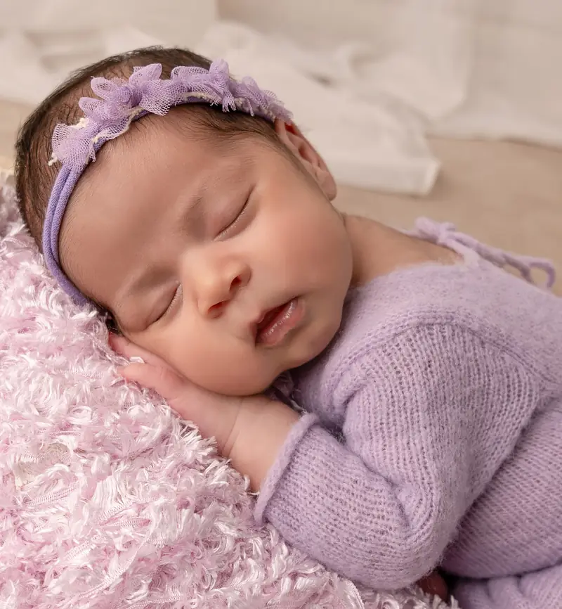 Recién nacida dormida con vincha de flores lilas sobre una manta rosada