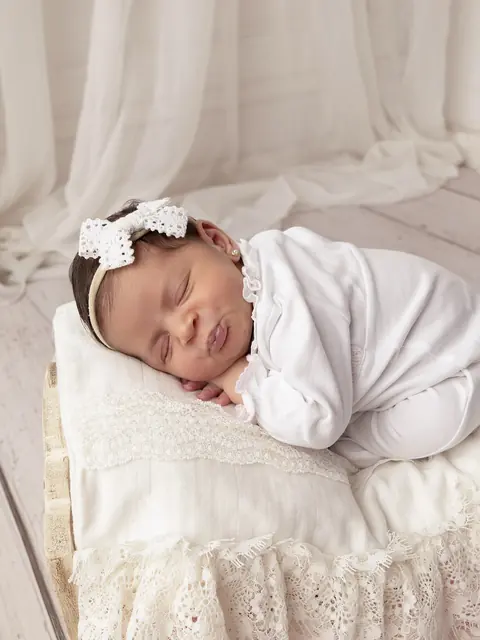 Recién nacida con moño blanco sobre una almohada de encaje