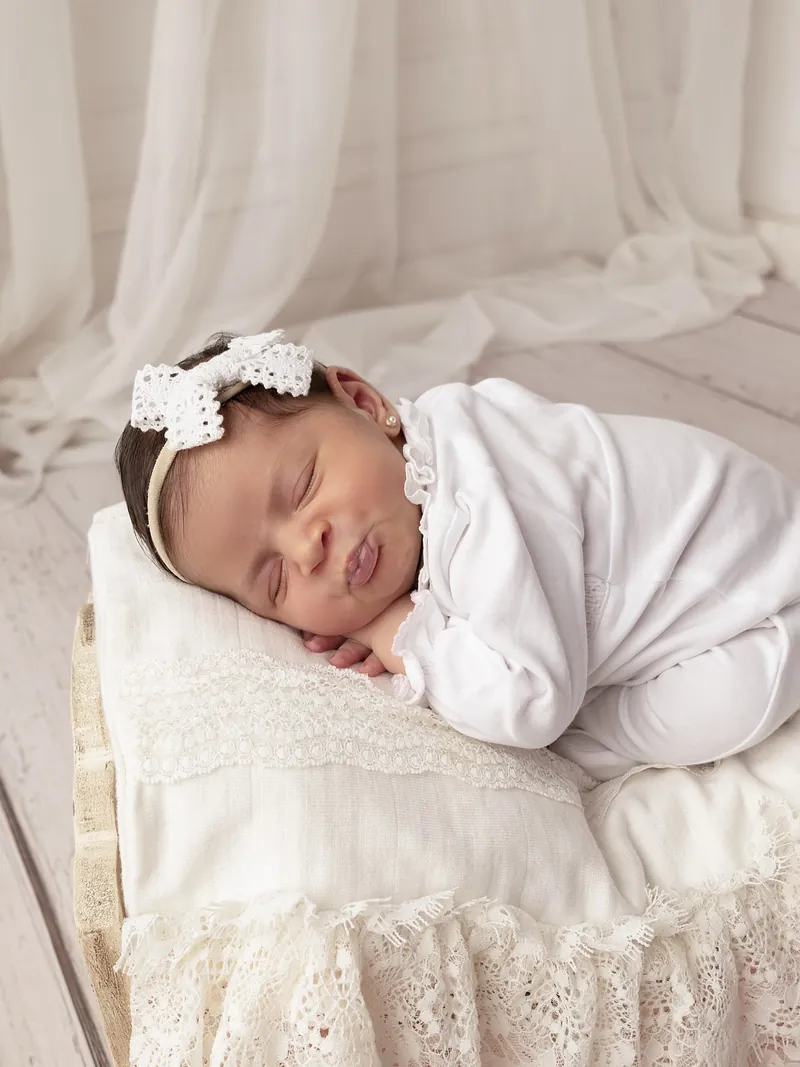 Recién nacida con moño blanco sobre una almohada de encaje