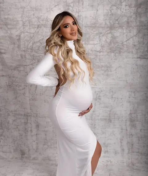 Embarazada de perfil con vestido blanco, tomándose la panza