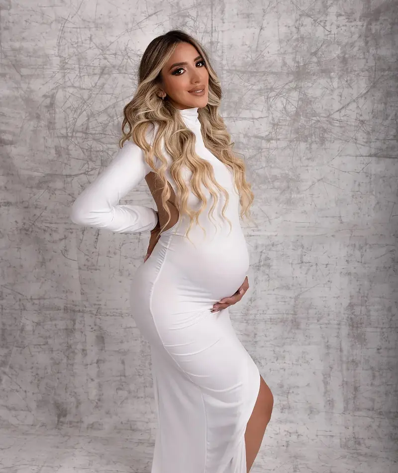 Embarazada de perfil con vestido blanco, tomándose la panza