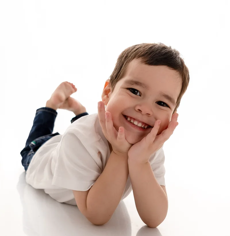 Niño sonriente acostado en el piso con las manos en la cara