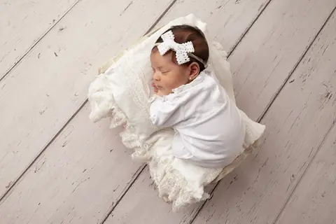 Recién nacida dormida de costado con un moño blanco