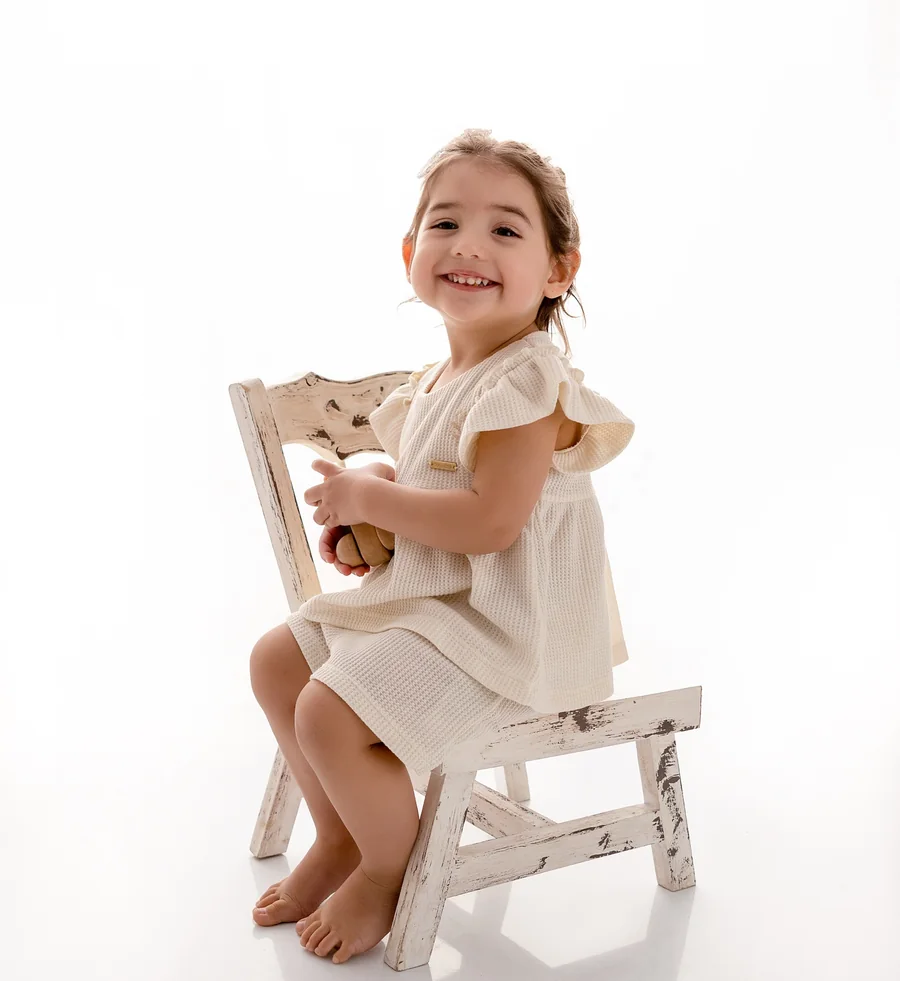 Niña sonriente sentada en una sillita blanca